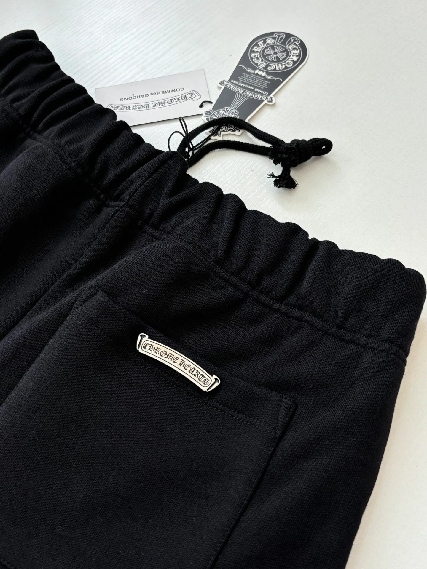 P346 Chrome Hearts*/Chrome Hearts 26SS early spring new patch embroidered shorts The fabric is made of a blended ratio of 80% cotton and 20% polyester. It is woven with a siro spinning process of 32-count base yarn and 10-count veil to form a high-weight terry cloth base of 380g/㎡. The cotton-polyester blended material combines the skin-friendly breathability of cotton and the anti-wrinkle shape retention of polyester. The high-weight fabric gives the trousers excellent stiffness and drape. The core technology is patch embroidery, which is completed with the help of TAJIMA computer embroidery machine. The black special-shaped patch is precisely sewn to the trouser fabric through lock stitches. The embroidery stitch density is even and the edges are neatly hemmed, forming a three-dimensional relief-like visual effect. Size: S/M/L/XL